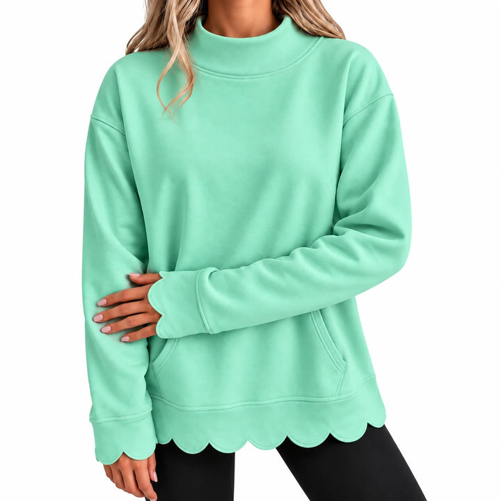 Close-up of the mint green pullover showing a raised neckline, shoulder seams, front pocket and scalloped hem and sleeve ends