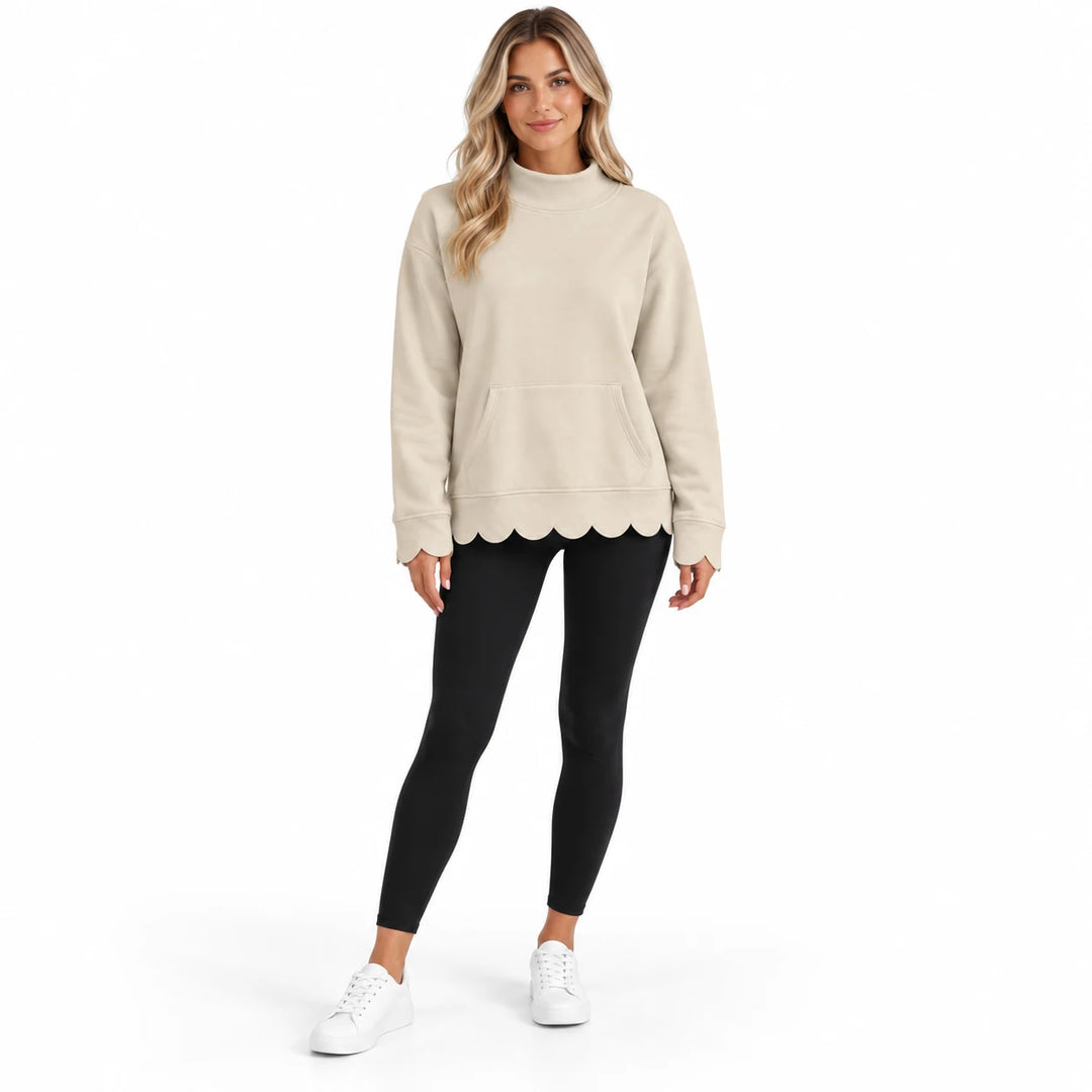 Full-body model in the sand beige pullover with long sleeves, a center kangaroo pocket and scalloped cuffs and hem, on white.