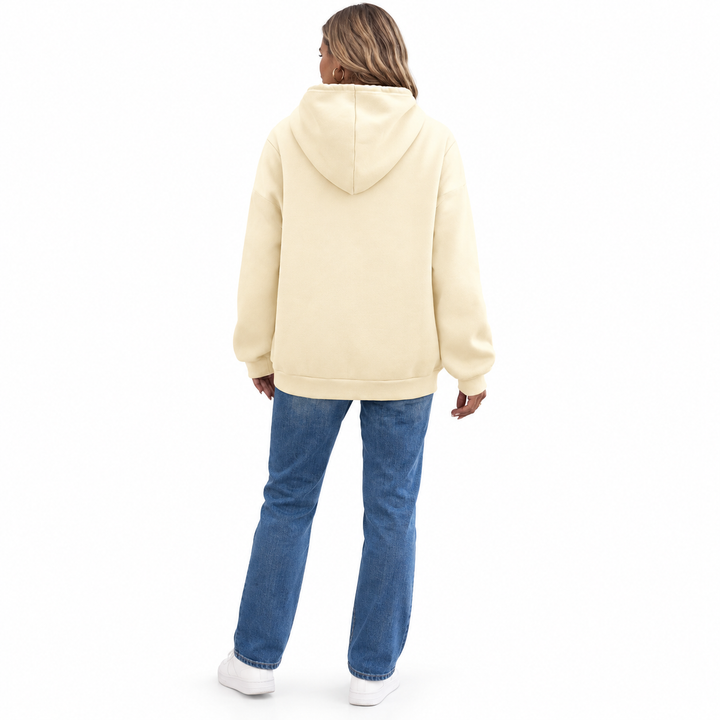 Rear view of a model in a cream hoodie with a plain back and ribbed hem, blue jeans and white sneakers on a white background.