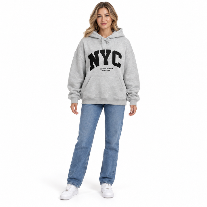 Full body model in a heather gray hoodie with NYC lettering, blue jeans and white sneakers against a white studio background.