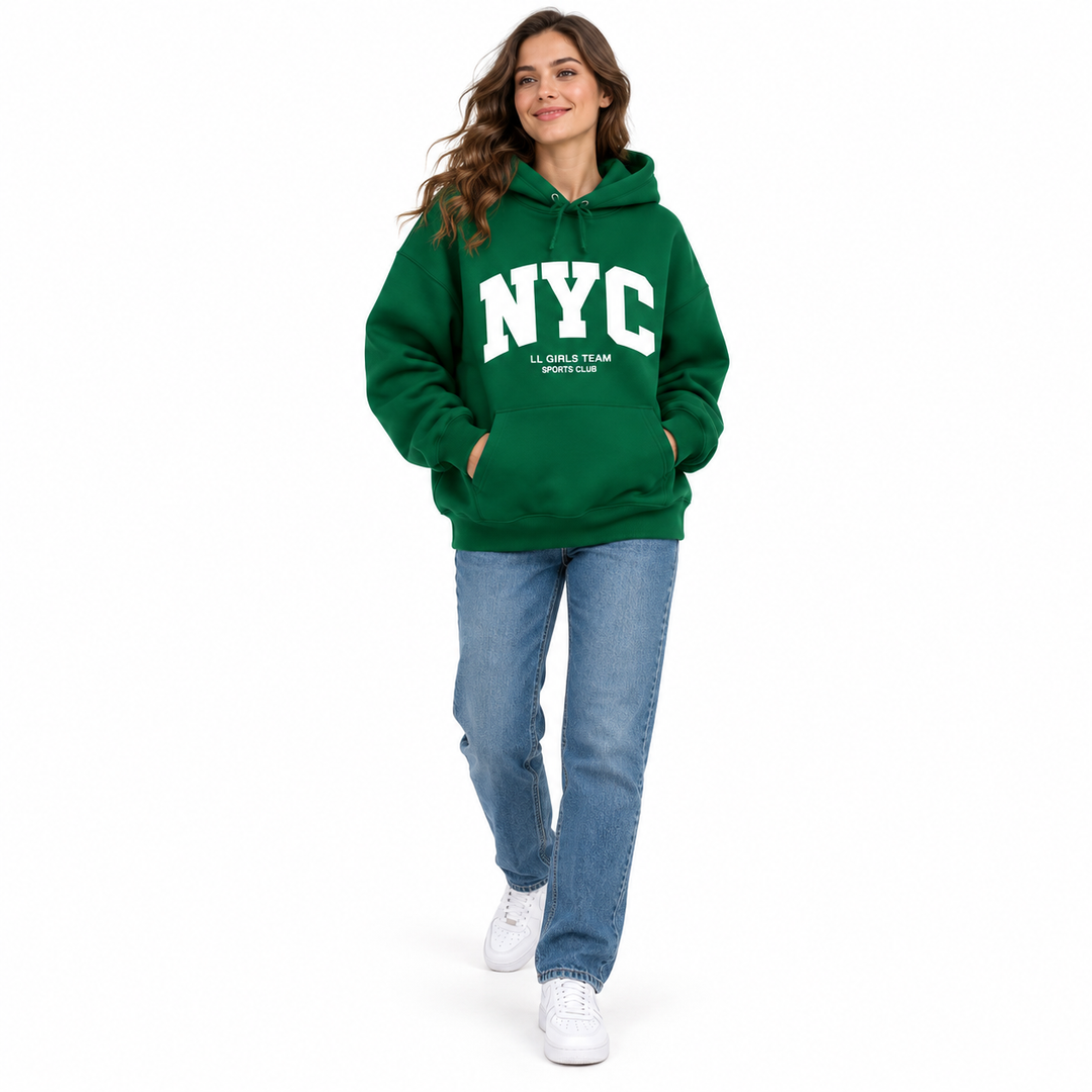 Full body model in a forest green hoodie with NYC lettering, blue jeans and white sneakers against a white studio background.
