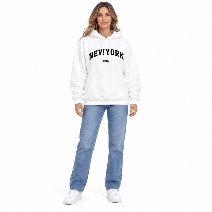 Full body model in a white hoodie with New York USA graphic print, blue jeans and white sneakers on a plain white background.