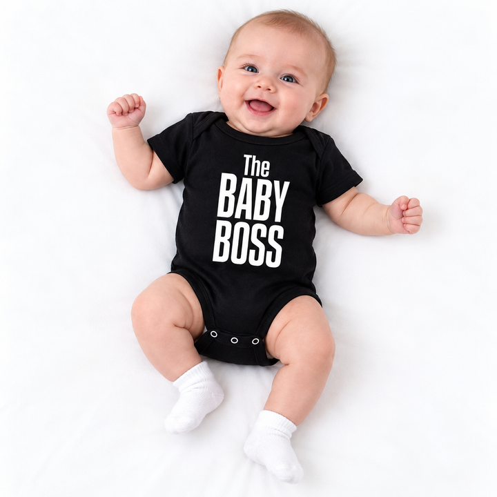 Baby lying on white studio surface wearing a black The Baby Boss printed short-sleeve romper, with head and feet in full view