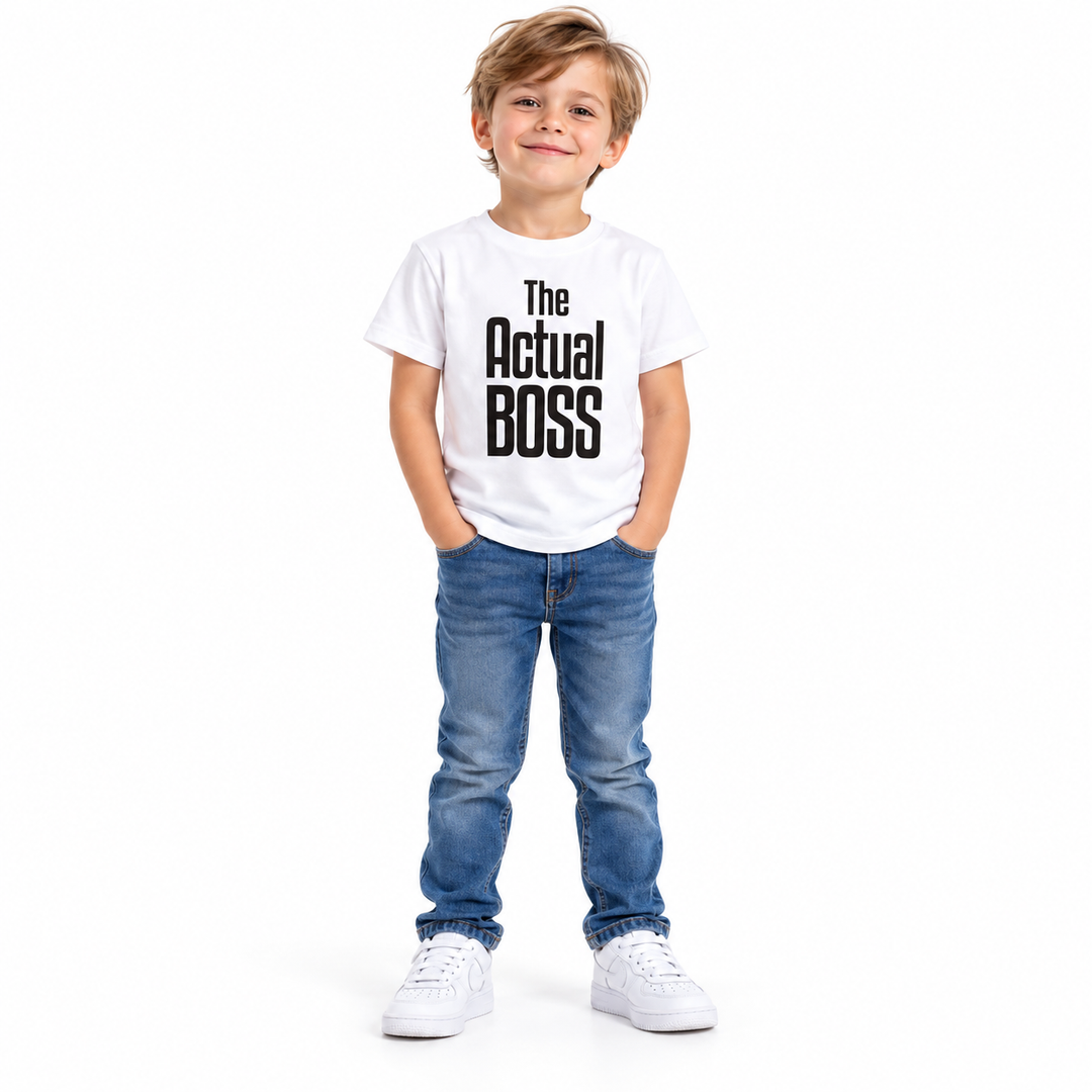 Full-body child wearing a white The Actual Boss printed T-shirt, blue jeans and white sneakers against white studio backdrop.