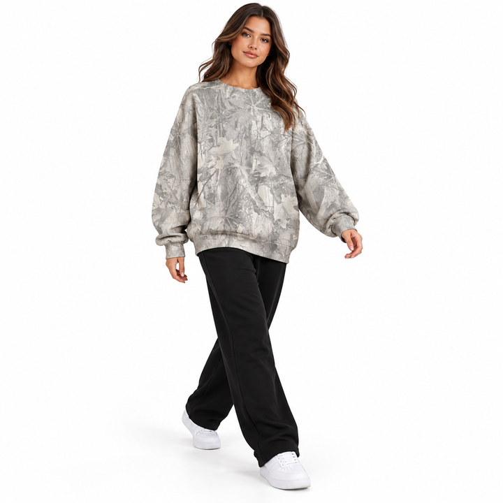 Model wearing a grey branch print sweatshirt in a full-body walking pose with trousers and shoes on a plain white background.