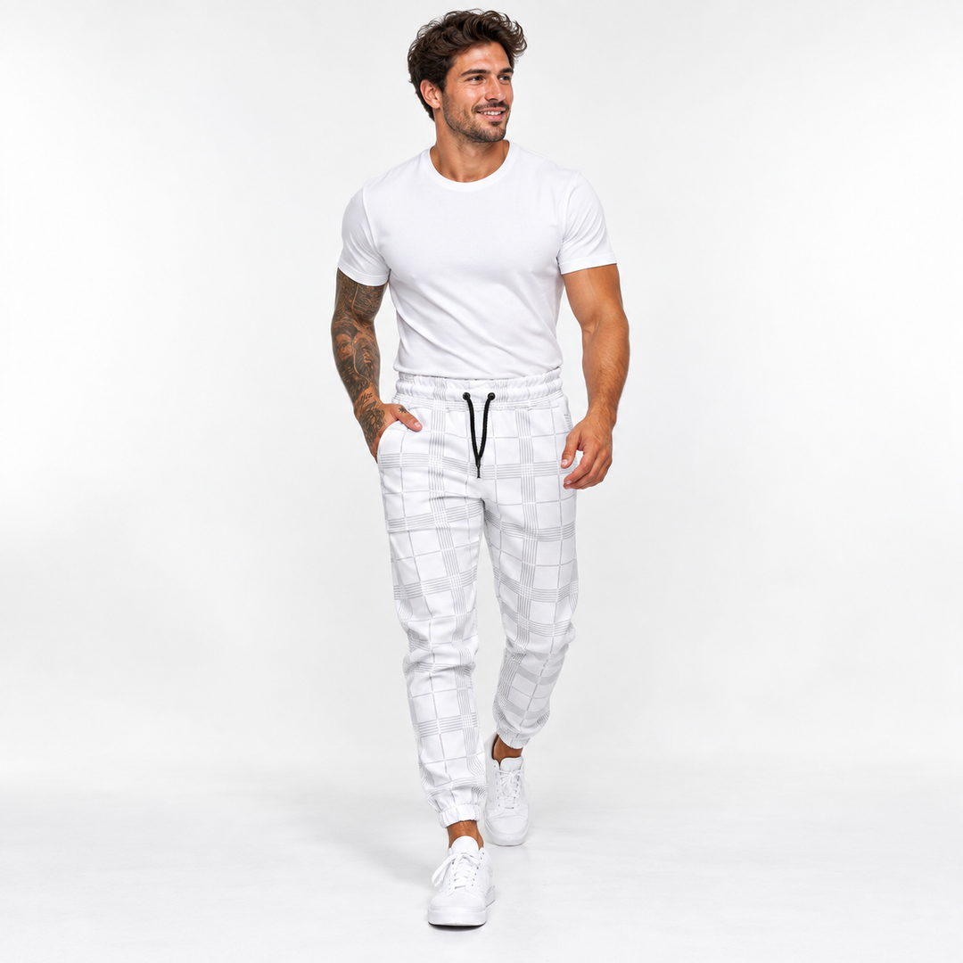 Plaid pants for men in white on male model walking in studio, showing tapered jogger shape, black drawstring and ankle cuffs.