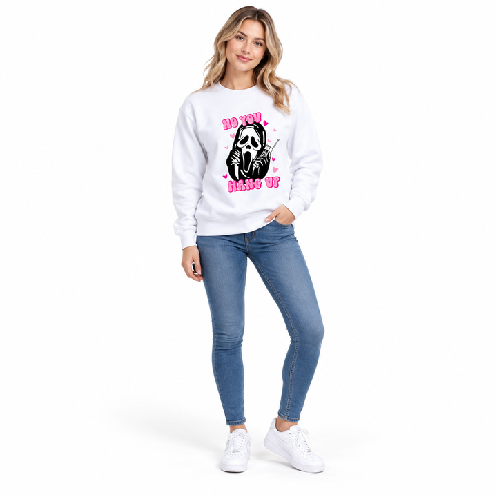 Woman wearing a white graphic pullover with pink lettering, a black phone graphic and ribbed cuffs in a white studio setting.