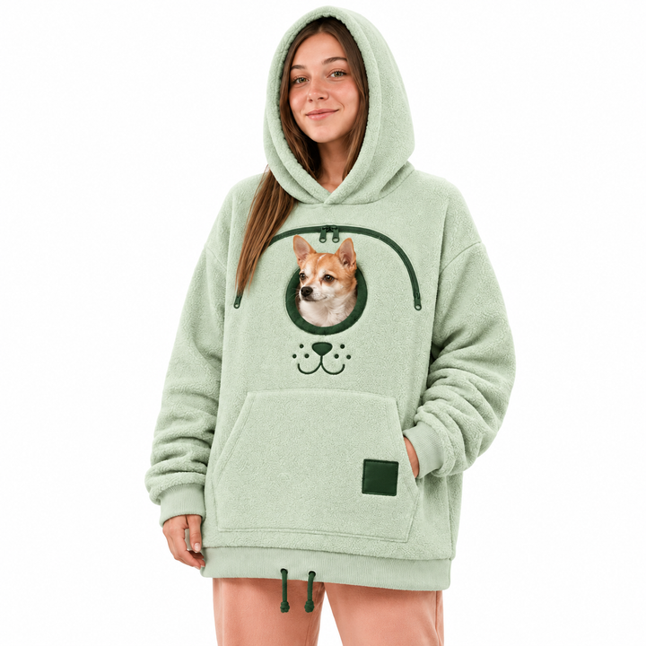Woman wearing a light green hooded pullover with a green zipper, real small dog and a front pocket in a white studio setting.