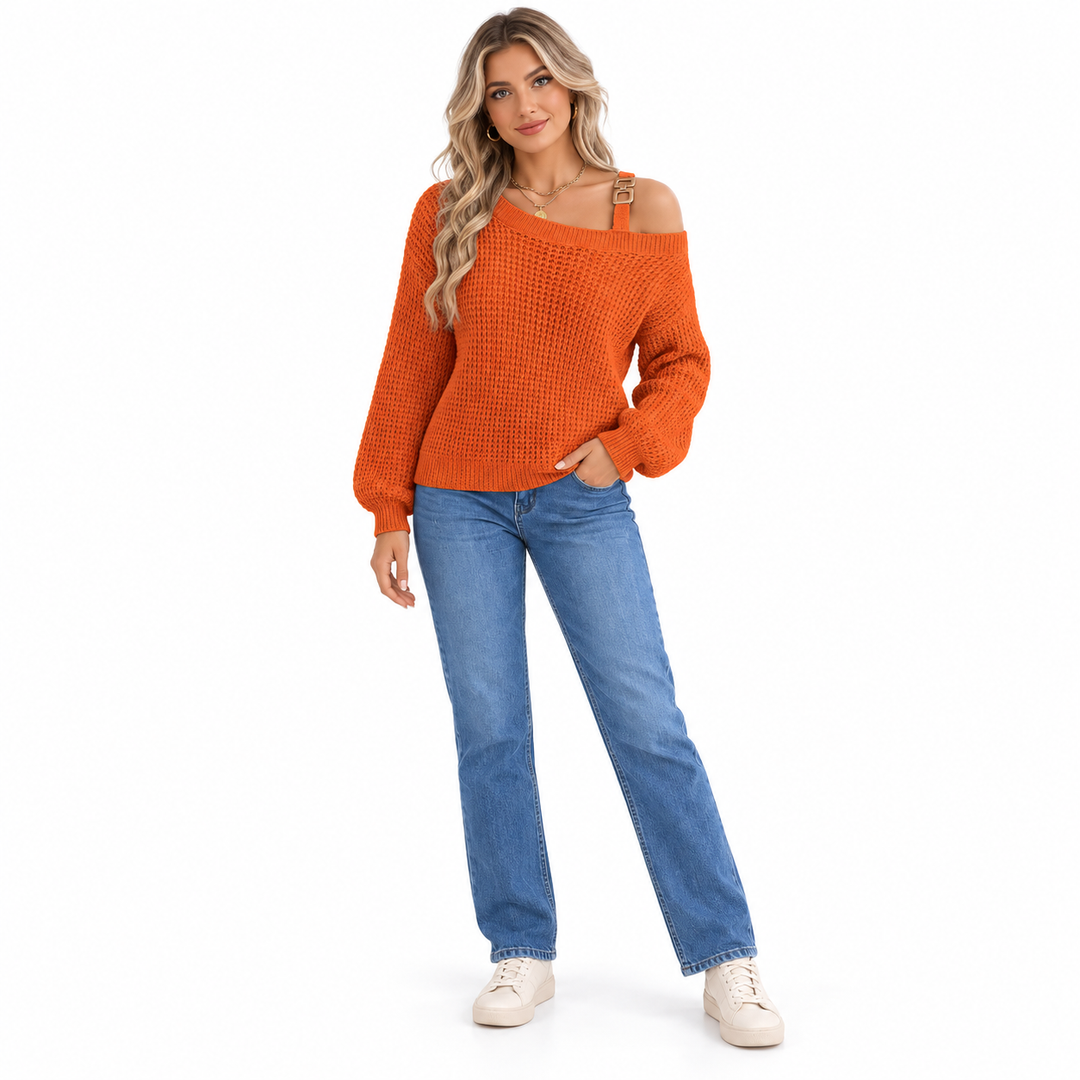 Orange knit sweater with a metal buckle shoulder strap and lantern sleeves, worn with blue jeans on a woman in a white studio