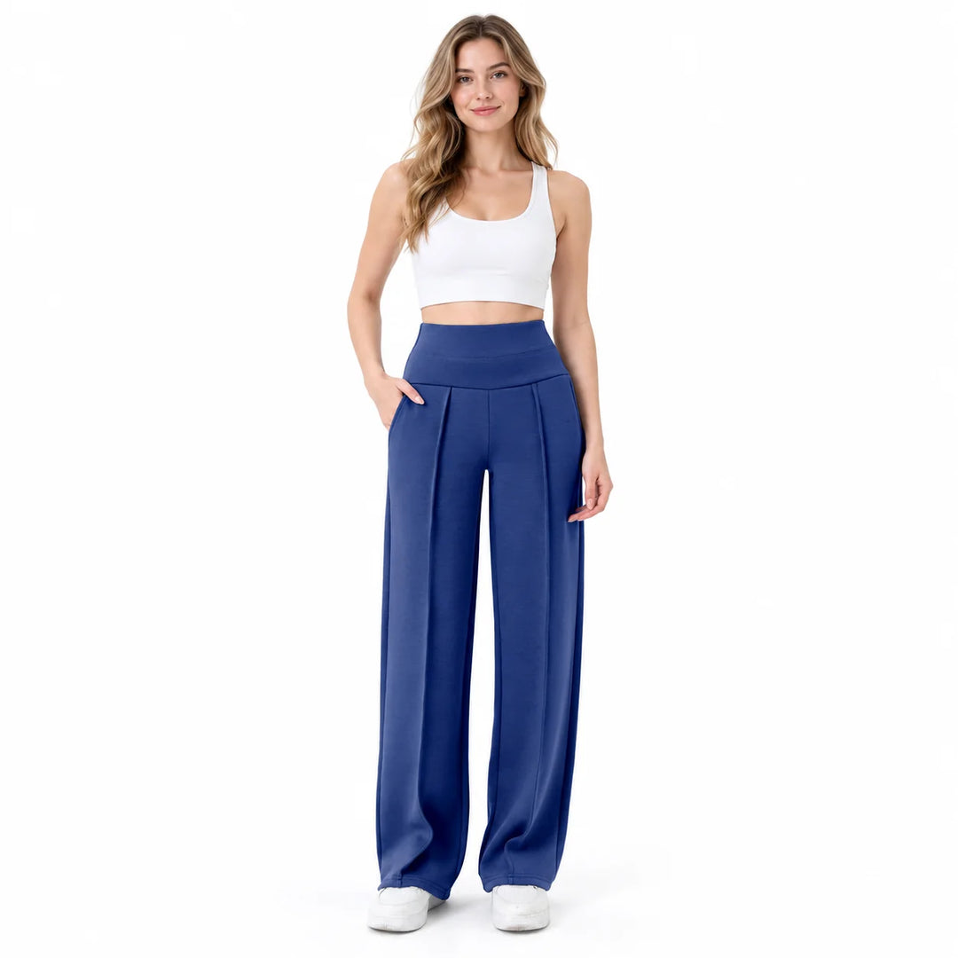 Straight leg yoga pants in blue on a full-body model, showing high waistband, front pleats and pockets against a white studio