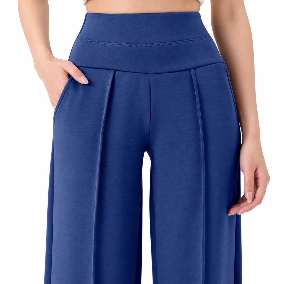 Straight leg yoga pants in blue shown close up, with a broad stitched waistband, front pleats and curved side pocket visible.