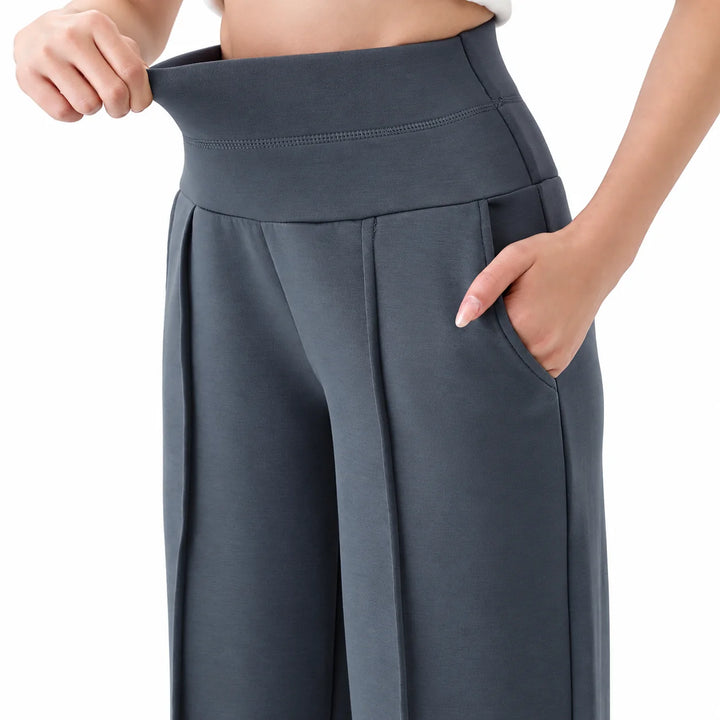 Dark gray athletic trousers shown close up with a hand in the curved pocket, beside the broad waistband and front pleat seam.