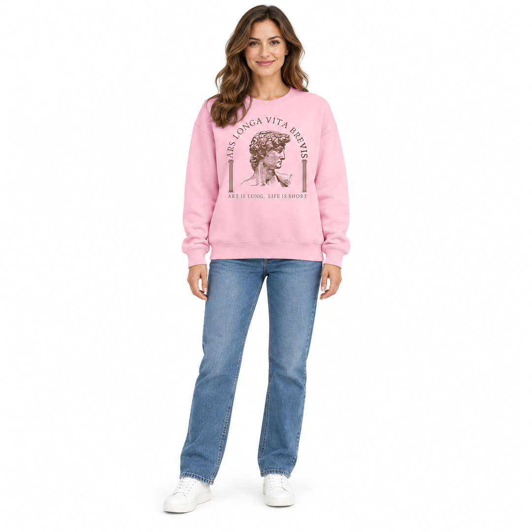 Pink round neck sweatshirt on full-length female model, showing the brown sculpture print, blue jeans and white studio shoes.