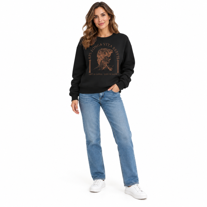 Black sweatshirt on full-length woman in a slight front angle, with brown art print, blue denim jeans and white studio shoes.