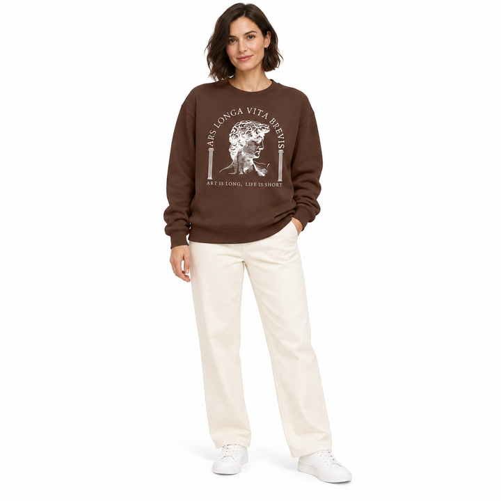 Coffee brown sweatshirt with white sculpture print on a second full-length woman, styled with ivory trousers and white shoes.