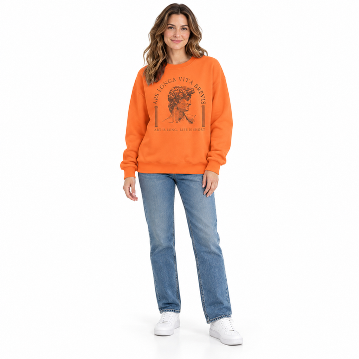 Orange sweatshirt on a full-length woman with brown sculpture print, dropped shoulders, blue jeans and white shoes in studio.