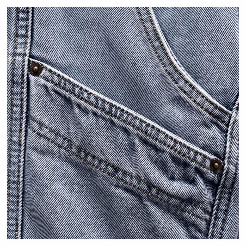 Close view of washed blue denim fabric, curved pocket stitching and a metal rivet, showing the blue jacket&