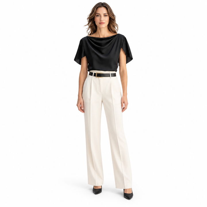 Front view of model in a black blouse with draped neckline and short sleeves, ivory trousers and heels on a white background.