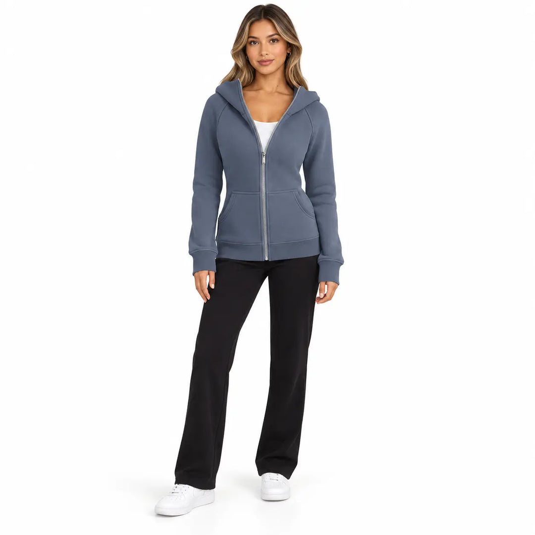 Full-body model wearing the Slate Blue zip hoodie, showing front pockets, ribbed cuffs and hem, on white with black trousers.