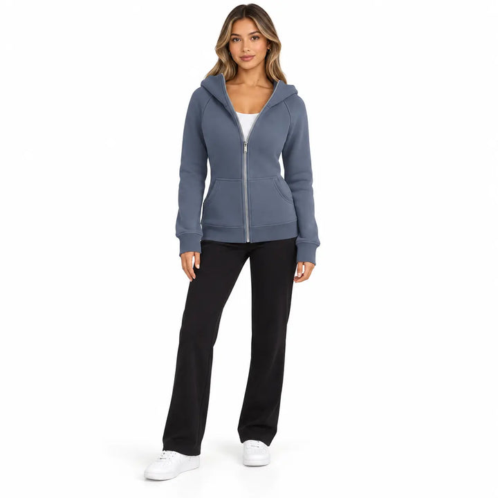 Full-body model wearing the Slate Blue zip hoodie, showing front pockets, ribbed cuffs and hem, on white with black trousers.