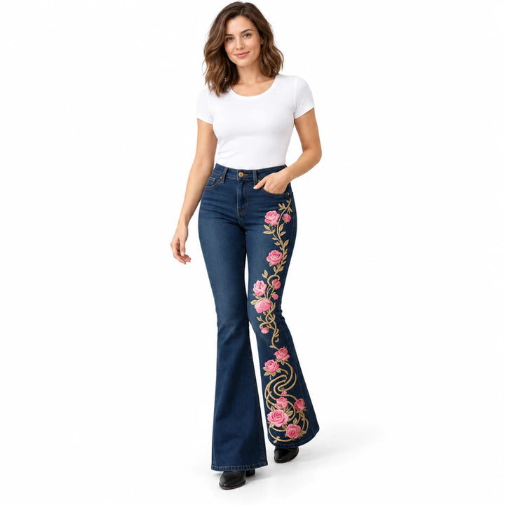 Model taking a step in dark blue floral flare jeans with pink roses and gold-tone scroll print on one leg, on white.
