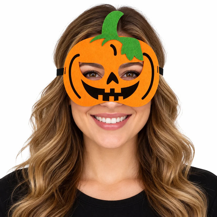 Adult woman wearing an orange pumpkin Halloween eye mask with black smile and green stalk, photographed on a white background