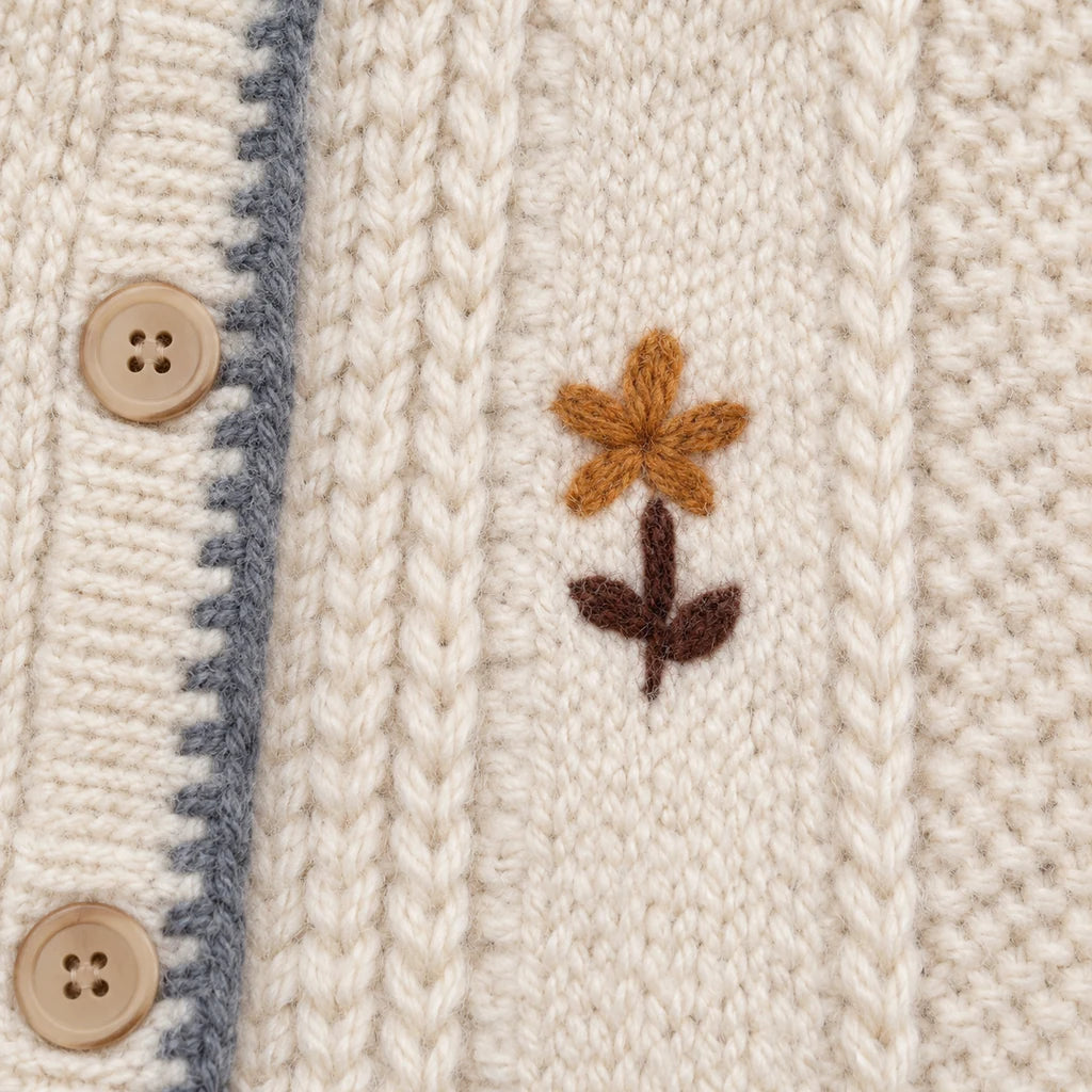 Close-up of ivory knit and an embroidered ochre flower with a dark stem, showing front texture of the floral button cardigan.