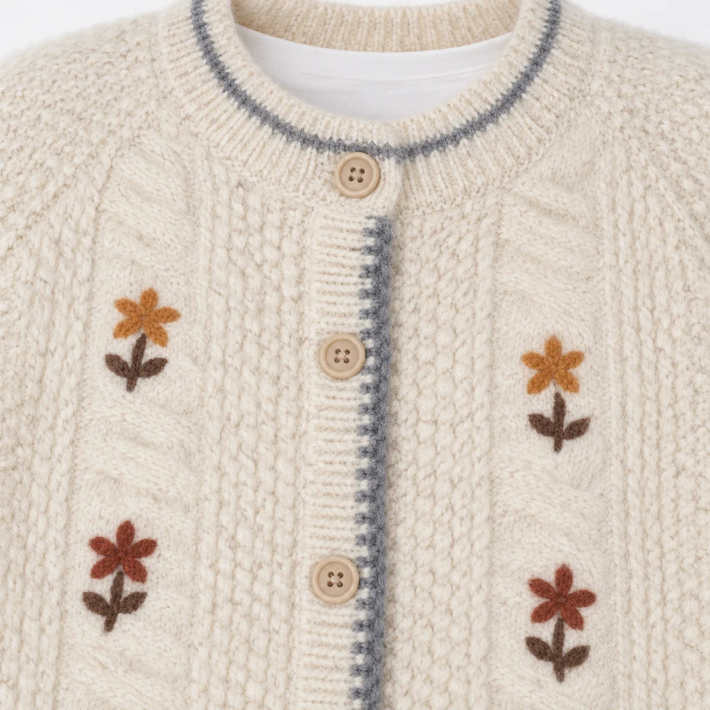 Close-up of the ivory cardigan round neckline and beige button placket, with gray edging and front texture and floral detail.