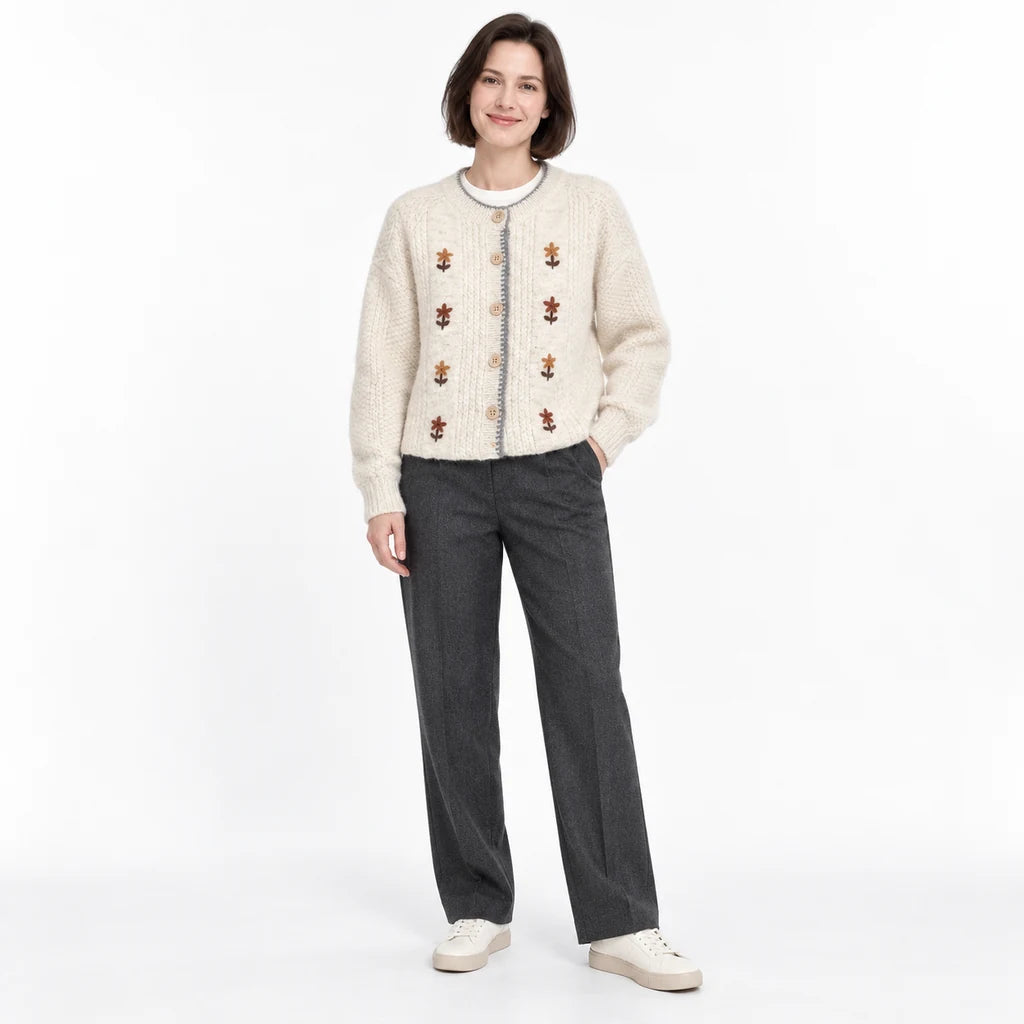 Ivory floral cardigan on a second full-length model with a dark bob, styled with a white top, charcoal trousers and sneakers.