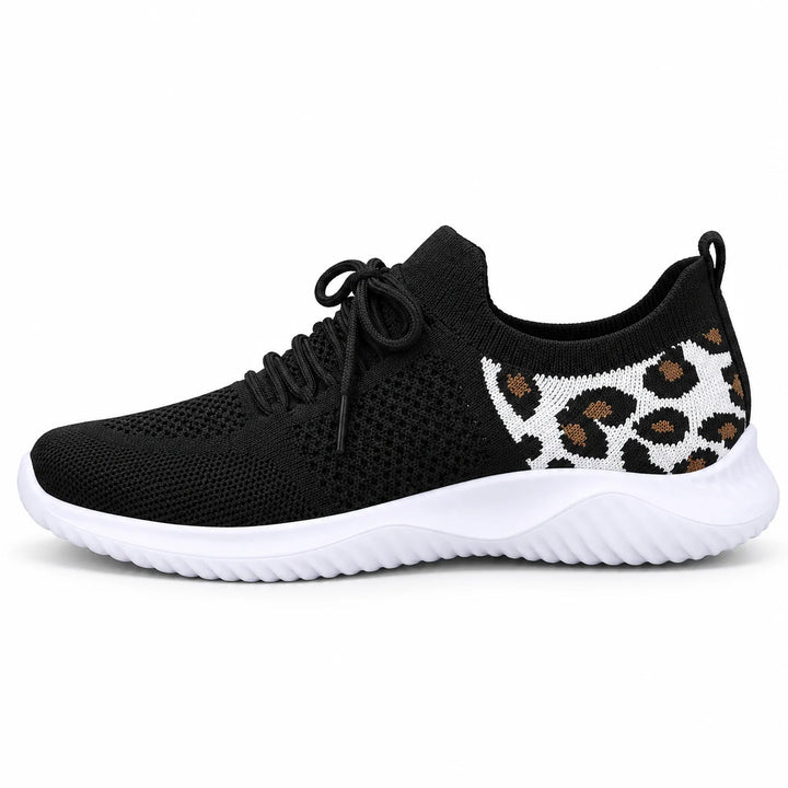 Side view of a black mesh lace-up sneaker with a white sole and tan leopard heel panel, photographed against a white setting.