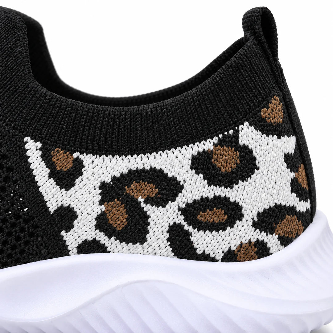 Close view of a white knitted heel panel with black and tan leopard spots, a black collar above and white sneaker sole below.