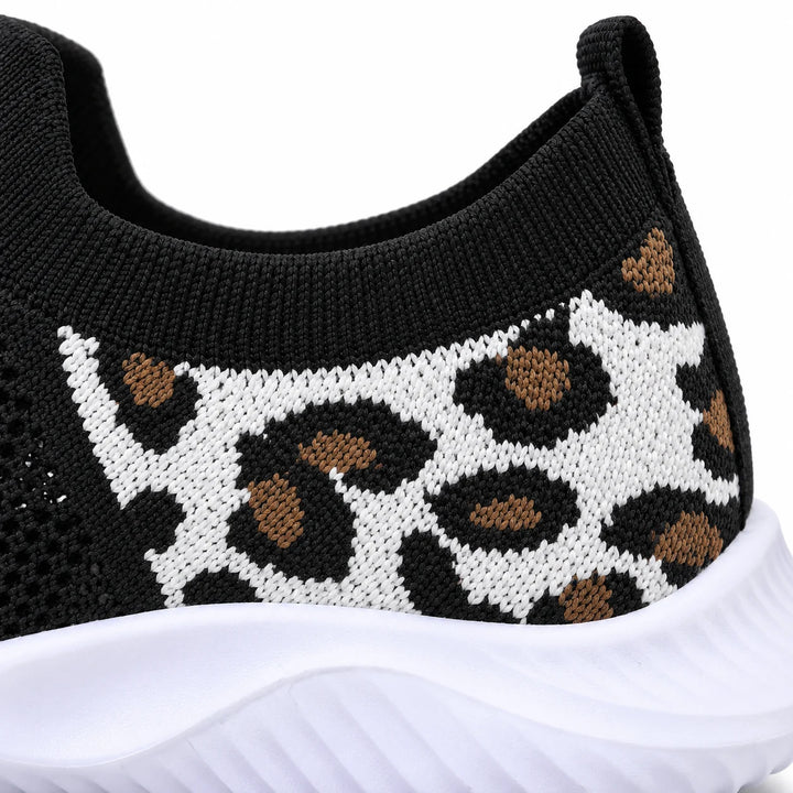 Close view of a white knitted heel panel with black and tan leopard spots, a black collar above and white sneaker sole below.