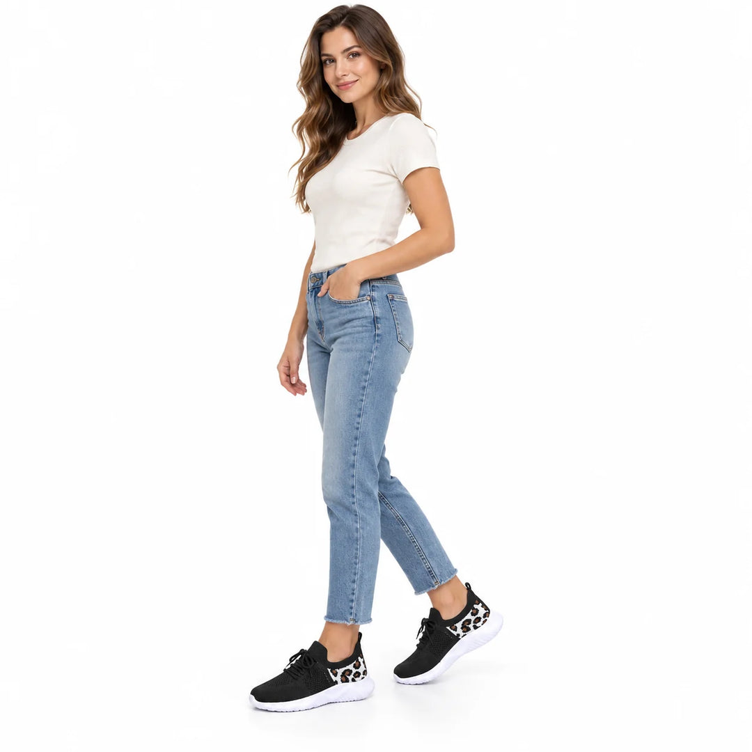 Woman in blue ankle jeans and an ivory top wearing black mesh sneakers with leopard heel panels, shown in a full body stance.