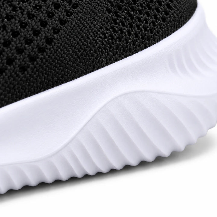 Close side view of the white sneaker sole with diagonal sculpted ridges and a small band of black knitted mesh along its top.