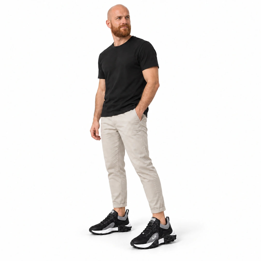 Full-body male model wearing Black and Gray sneakers with a black T-shirt and light trousers against a white studio backdrop.