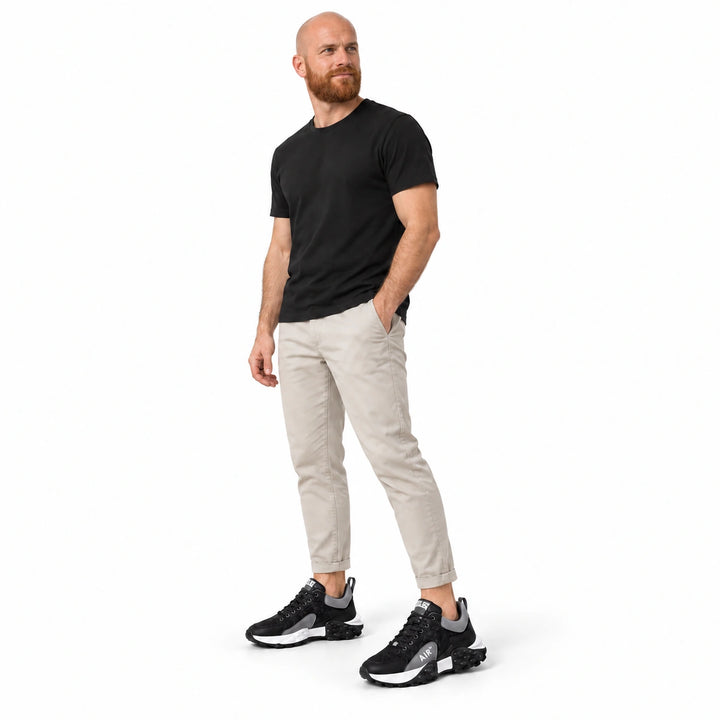Full-body male model wearing Black and Gray sneakers with a black T-shirt and light trousers against a white studio backdrop.