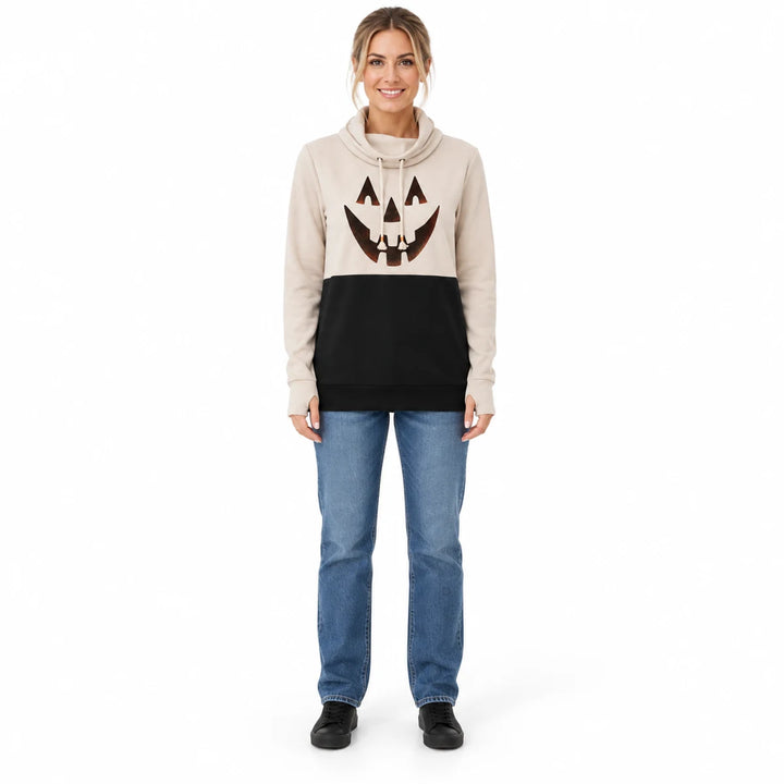 Woman wearing a beige and black pumpkin top with jeans and black shoes, shown in a full-body front view against a white wall.