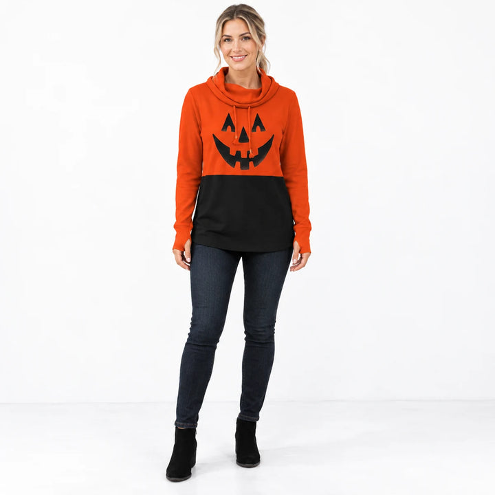 Woman wearing the pumpkin orange and black printed pullover with dark jeans and black shoes in a bright minimal studio photo.