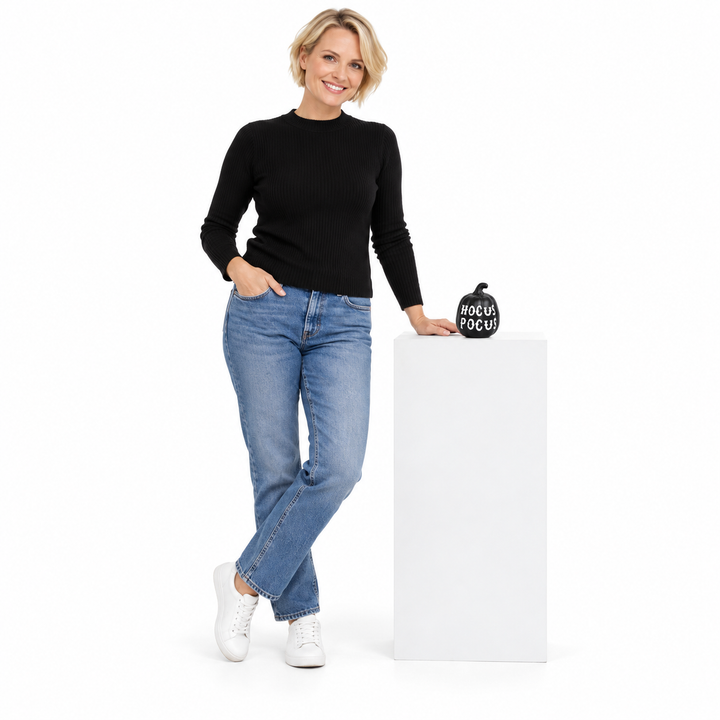 Adult blonde woman beside a white pedestal displaying the black HOCUS POCUS pumpkin, shown in full in a white studio setting.
