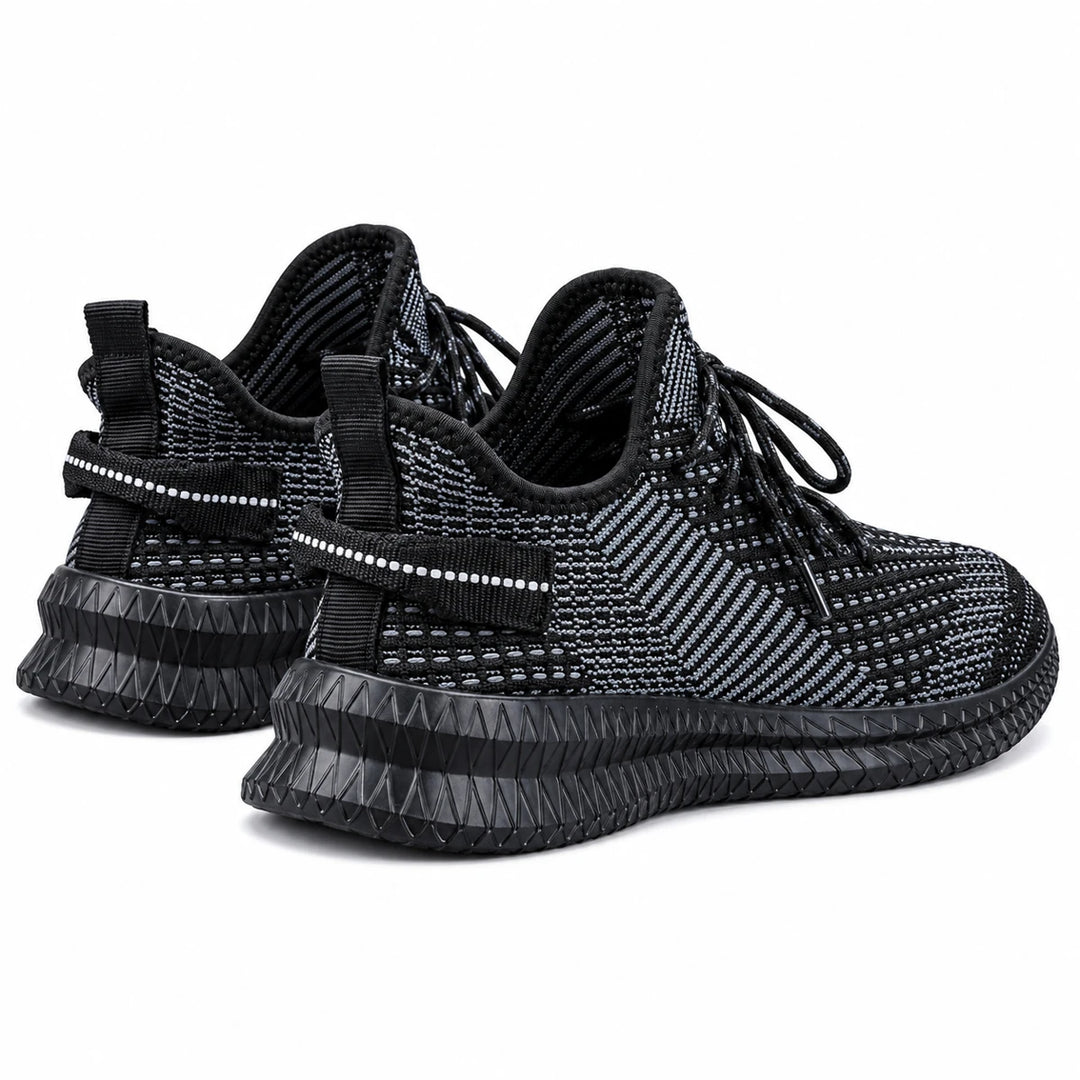 Black mesh sneakers shown from a rear-quarter angle, with heel pull tabs and sculpted soles on a plain white studio backdrop.