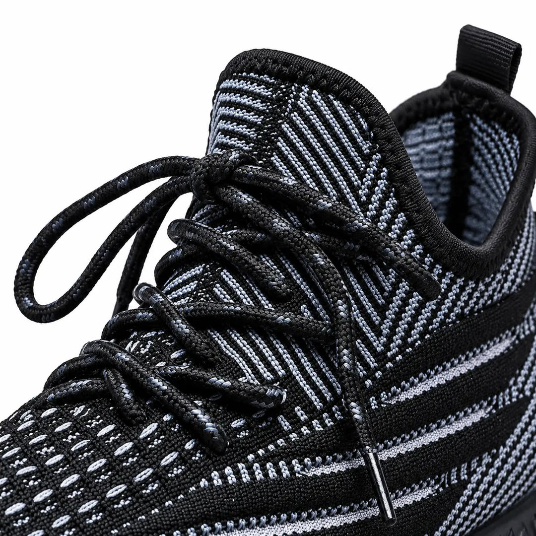 Close view of black sneaker laces, tongue &amp; pull tab, with the patterned mesh upper visible on a plain white studio backdrop.