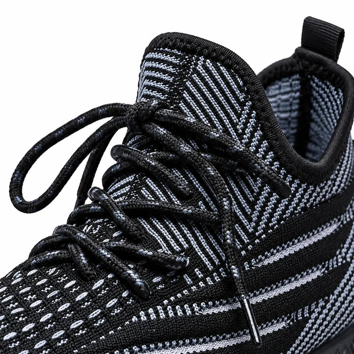 Close view of black sneaker laces, tongue &amp; pull tab, with the patterned mesh upper visible on a plain white studio backdrop.