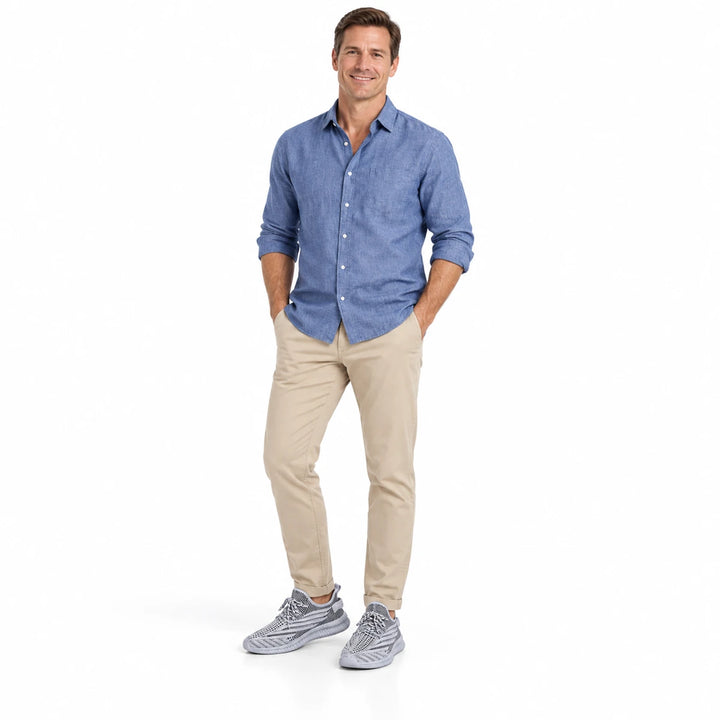 Adult male model wearing Gray mesh sneakers with neutral trousers and a plain blue shirt with white space around the subject.