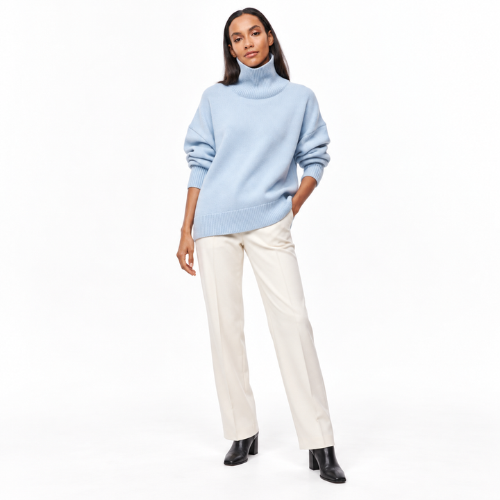 Full-length model wearing a light blue turtleneck sweater styled with ivory tailored trousers and black ankle boots on white.