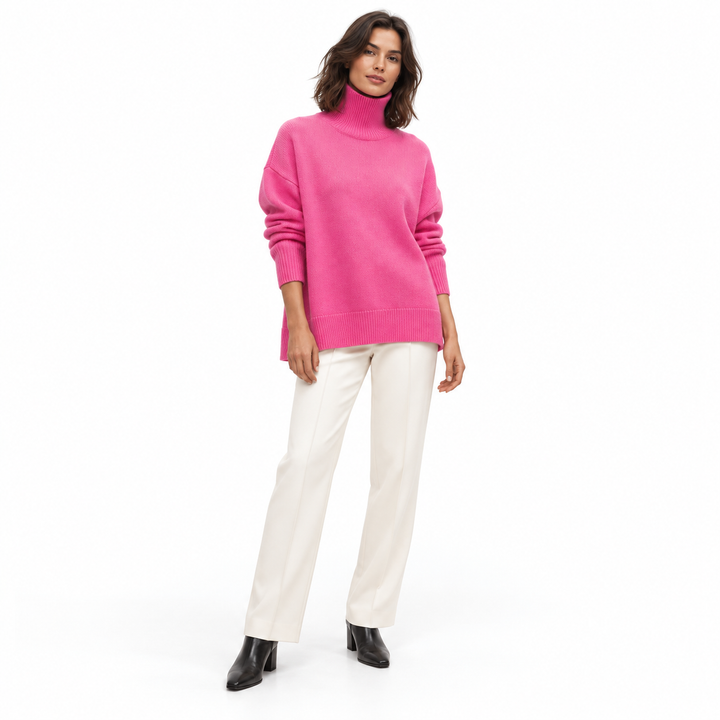 Full-length model wearing a rose red turtleneck sweater with ivory trousers and black ankle boots against a white background.