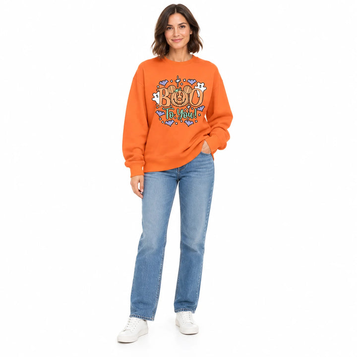 Orange crewneck sweatshirt with the Boo To You pumpkin print on a brunette adult model with jeans and sneakers against white.