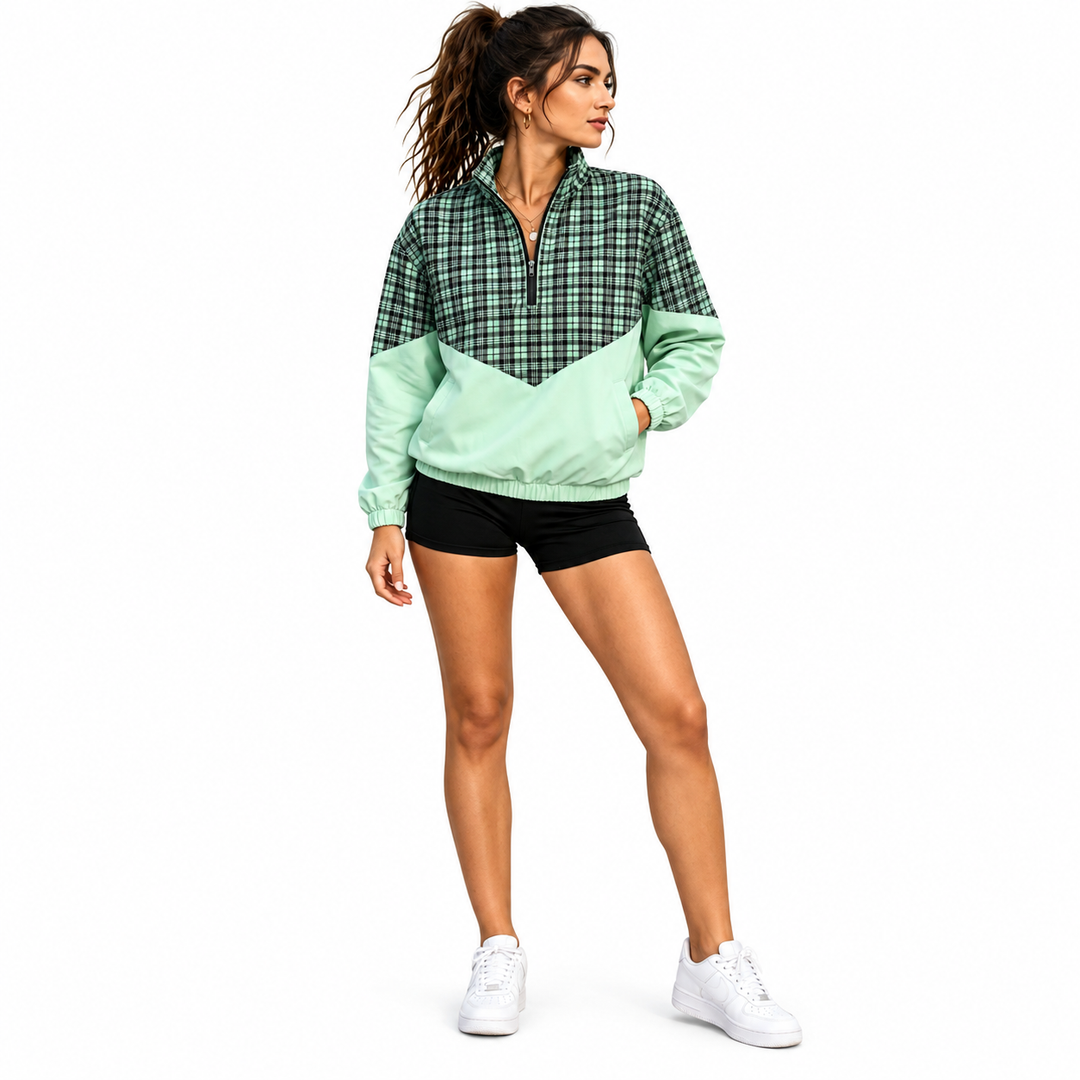 Woman wearing mint green and black plaid pullover jacket with half zipper, black shorts and white trainers in full-body view.