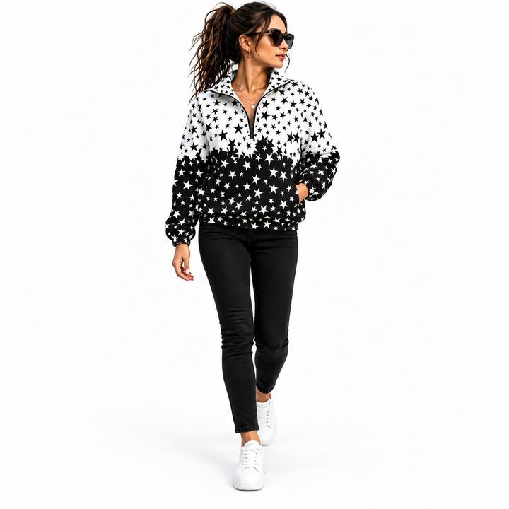 Woman wearing a black and white star printed jacket with black jeans and white sneakers, shown walking in white studio space.