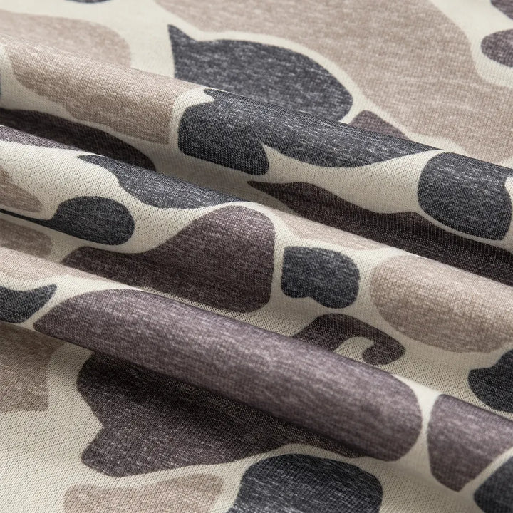 Close-up of folded camouflage fabric, showing the cream base, charcoal and taupe patches, fine knit texture and natural folds