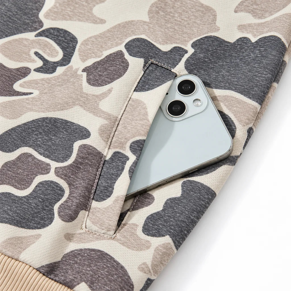 Front welt pocket detail with a phone inside, showing pocket stitching and charcoal and taupe camouflage fabric against white